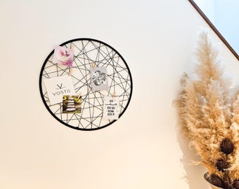 May include: A black metal wire circle wall decor with a variety of cards pinned to it. The cards have different designs and text, including a logo for "Vostil", a photo of stacked stones, and a quote about being wonderful. The wall decor is hanging on a white wall with a dried pampas grass arrangement in the background.