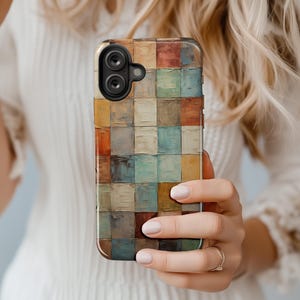 May include: A smartphone case with a colorful, abstract design. The case features a pattern of small, square blocks in shades of brown, orange, blue, and cream. The phone case has a camera and flash.