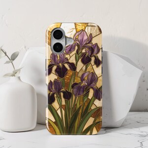 May include: A rectangular phone case featuring a stained glass pattern of purple iris flowers with green stems and leaves against a background of amber and cream geometric shapes. The case has a cutout for a dual camera lens on the upper left side.