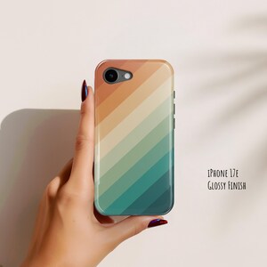 May include: A phone case for an iPhone 17E with a glossy finish, featuring a diagonal striped pattern in gradient shades of orange, beige, and teal. The design covers the entire back of the case, which includes a circular cutout for the camera lens.