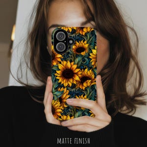 May include: A smartphone case featuring a vibrant pattern of yellow sunflowers with dark brown centers, set against a background of swirling dark teal and green foliage. The case has a matte finish and includes a cutout for a dual camera system.