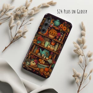 May include: A glossy black phone case featuring a detailed illustration of a wooden shelf filled with pumpkins, flowers, and teapots. The case has a camera cutout and the text "S24 PLUS IN GLOSSY". Decorative dried plants are in the background.