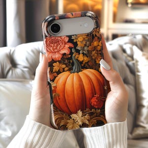 May include: A smartphone case featuring a vibrant orange pumpkin as the central focus, surrounded by detailed illustrations of autumn leaves, golden yellow flowers, and deep red blossoms set against a dark, moody black background.
