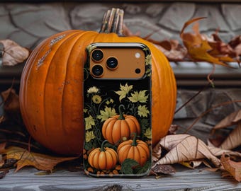 May include: A black smartphone case featuring a graphic illustration of three orange pumpkins surrounded by yellow and green autumn leaves. The case has a solid orange camera module area and is positioned in front of a large, real orange pumpkin.