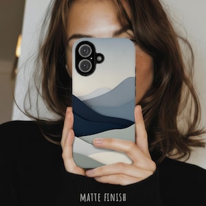 May include: A phone case with a matte finish featuring a layered landscape design in shades of navy blue, slate gray, light gray, and cream. The design consists of smooth, curved, overlapping shapes that create a mountain-like appearance.
