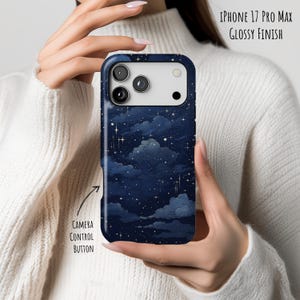 以下が含まれることがあります： 光沢仕上げのiPhone 17 Pro Max用ダークブルーのスマホケース。雲と星が描かれた夜空の模様が特徴です。カメラ部分の切り抜きと、カメラコントロールボタンを指し示すラベルが記載されています。