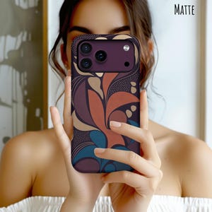 May include: A matte finish smartphone case featuring a dark purple camera module and a multi-colored abstract pattern of curved shapes in shades of terracotta, teal, beige, and dark purple, accented with fine stippled dot textures throughout.