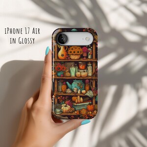 May include: An iPhone 17 Air in glossy case featuring a detailed illustration of a wooden shelf filled with autumn-themed items. The design includes pumpkins, flowers, and a teapot. The text "IPHONE 17 AIR IN GLOSSY" is printed on the case.