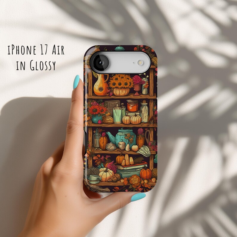 May include: An iPhone 17 Air in glossy case featuring a detailed illustration of a wooden shelf filled with autumn-themed items. The design includes pumpkins, flowers, and a teapot. The text "IPHONE 17 AIR IN GLOSSY" is printed on the case.