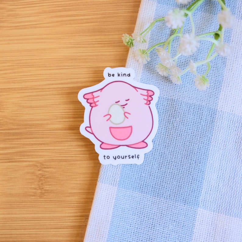 May include: Pink cartoon character holding a white egg with the text "be kind to yourself" on a white sticker.