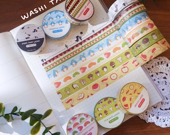 May include: A collection of decorative washi tape rolls featuring various patterns including pixelated dinosaurs, blue penguins, strawberries, mushrooms, and sliced fruits. The rolls are displayed on a grid notebook with strips of tape showing the designs.
