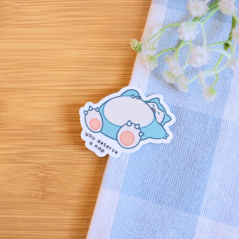 May include: A blue and pink sticker with a cartoon of a sleeping Pokemon character. The sticker says "You deserve a nap".