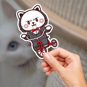 Könnte beinhalten: Ein weißer Katzenaufkleber mit rotem und schwarzem Design. Die Katze trägt einen Anzug und eine Fliege und fährt ein rotes Dreirad. Der Aufkleber befindet sich auf weißem Hintergrund.