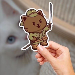 Puede incluir: Un gato de dibujos animados con un uniforme militar verde y un sombrero marrón con una estrella dorada. El gato sostiene una espada en su pata derecha y una espada más pequeña en su pata izquierda.