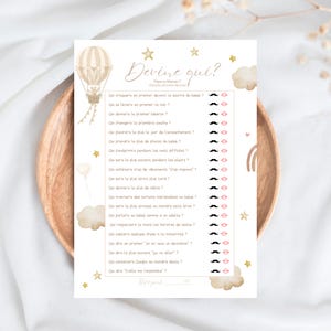 Peut inclure: Carte de jeu de baby shower avec le texte "Devine qui ?" en écriture élégante. La carte présente une illustration de montgolfière, des étoiles et des nuages. Le jeu comprend des questions sur le bébé et les parents.