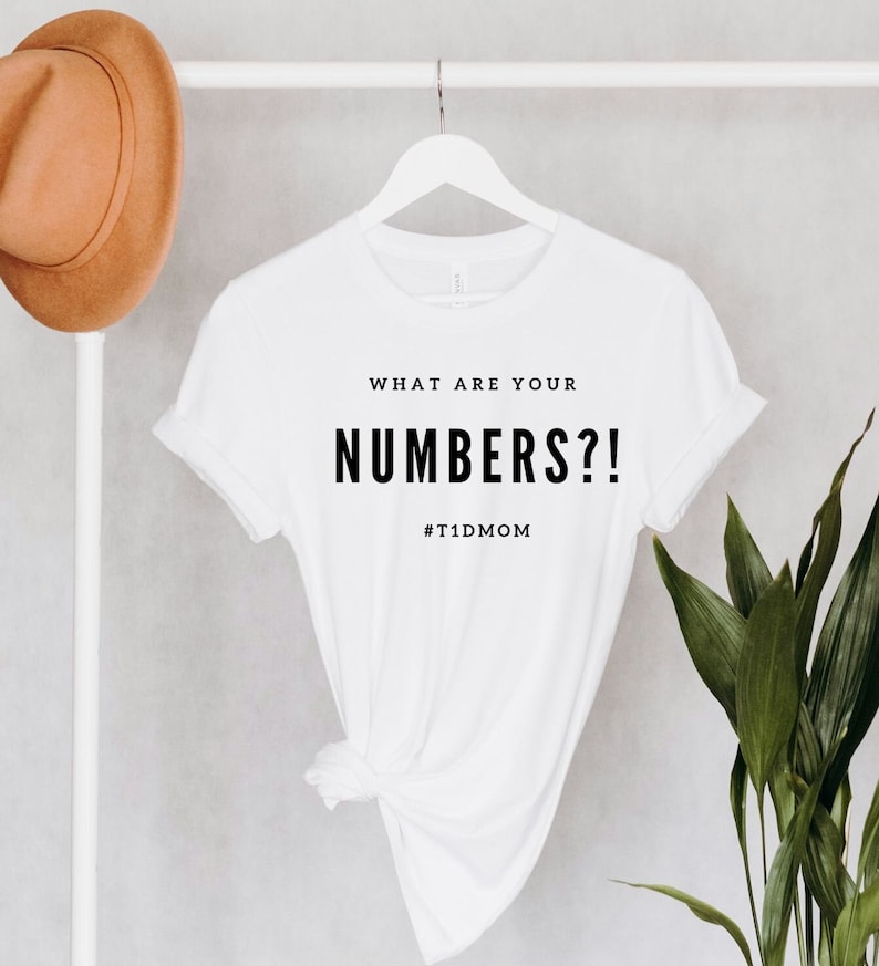 Pu&ograve; includere: Maglietta bianca con il testo "WHAT ARE YOUR NUMBERS?!" e l'hashtag "#T1DMOM" stampato in nero.