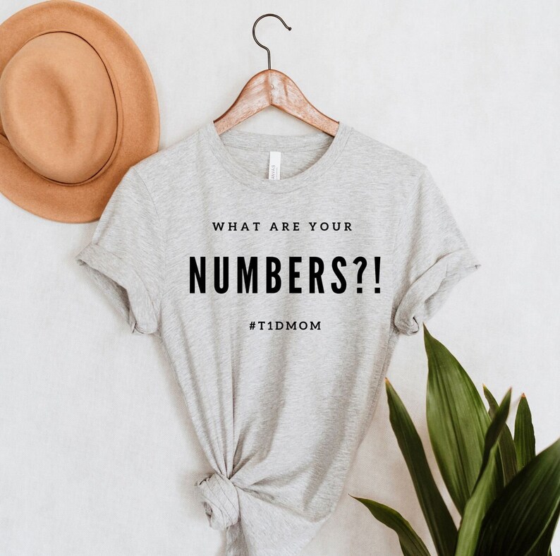 Pu&ograve; includere: Maglietta grigia con il testo "WHAT ARE YOUR NUMBERS?!" e l'hashtag "#T1DMOM" stampato su di essa.