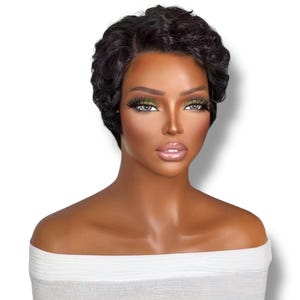 Op de afbeelding: Een korte, zwarte, golvende pruik met een zijscheiding op een etalagepophoofd. Het haar heeft strakke, gedefinieerde krullen die het gezicht omlijsten en een gestructureerde look creëren. De etalagepop heeft een gladde, gebruinde teint.