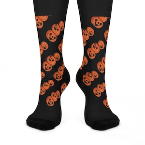 May include: A pair of black socks with a pattern of orange jack-o'-lantern faces. The socks are shown on a white background.