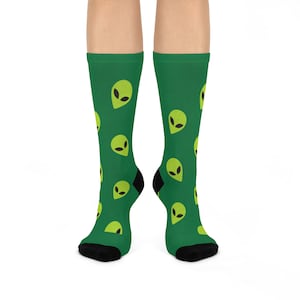 May include: A pair of green socks with a repeating pattern of yellow alien faces. The socks are black at the toes and heels.