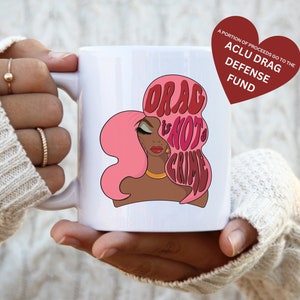 May include: White ceramic mug with a pink and red illustration of a woman with pink hair and the text "Drag is not a crime". A portion of proceeds go to the ACLU Drag Defense Fund.