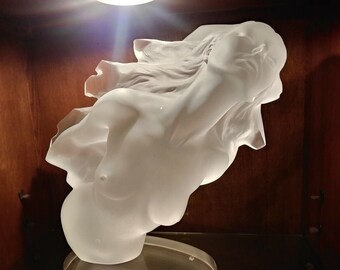Puede incluir: Escultura de cerámica blanca de un busto de mujer con la cabeza echada hacia atrás y el pelo suelto. La escultura está sobre una superficie de madera marrón oscuro.