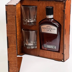 May include: Wooden gift box with a bottle of Gentleman Jack Tennessee Whiskey and two clear glasses. The box is open and the bottle is visible.