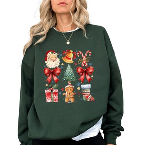 May include: Dark green sweatshirt featuring a festive Christmas design. The design includes Santa Claus, a bell, candy canes, a Christmas tree, red bows, gift boxes, a gingerbread man, and a Christmas stocking. The sweatshirt has a white crew neck.