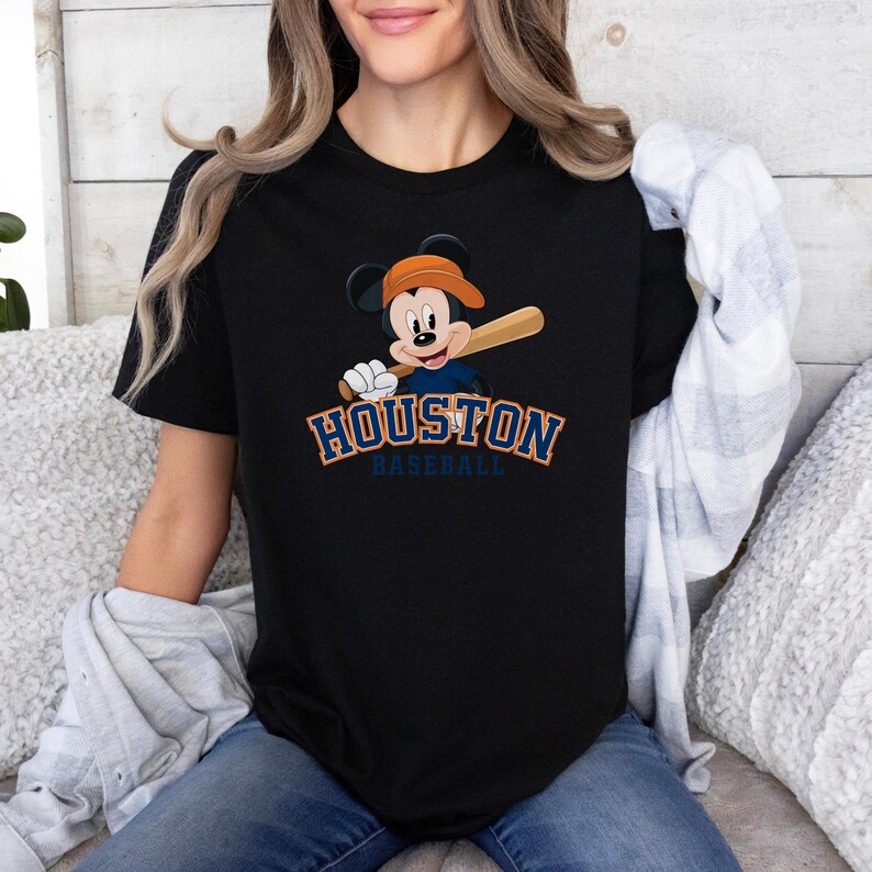 a woman sitting on a couch wearing a black shirt with a mickey mouse on it