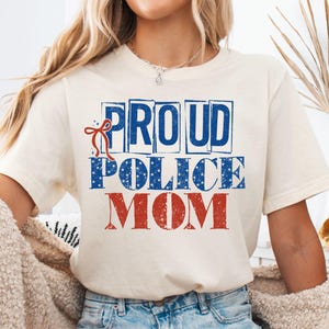 May include: A white ceramic mug with a black handle and the text "But First, Coffee" in a bold, black font. The mug is set against a blurred background, suggesting a cozy setting.