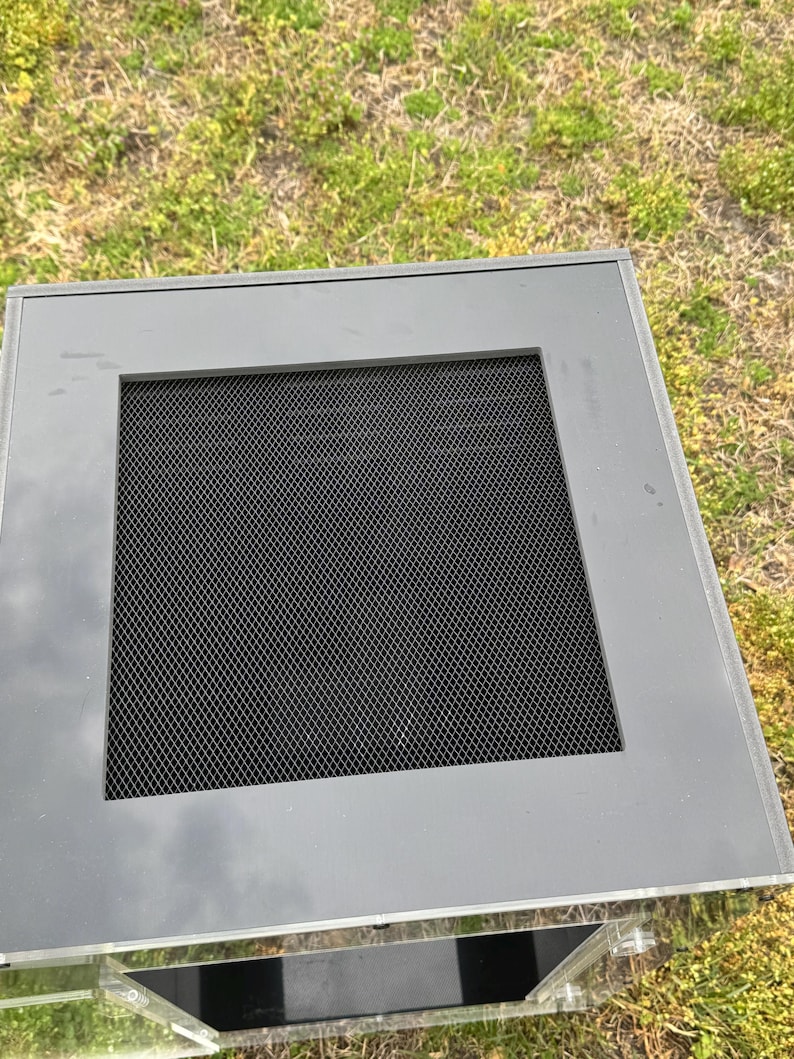 Op de afbeelding: Een grijze, rechthoekige vitrine met een zwart gaasscherm. De behuizing heeft een doorzichtige acryl behuizing en staat op gras. Het bovenste frame is effen grijs.
