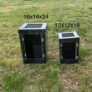 Op de afbeelding: Twee zwarte en zilveren reptielenverblijven. De grotere behuizing is 40.6x40.6x61 cm, en de kleinere 30.5x30.5x45.7 cm. Beide hebben een gaas bovenkant en een transparante deur. Ze staan op een grasachtige ondergrond.