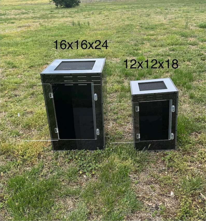Op de afbeelding: Twee zwarte en zilveren reptielenverblijven. De grotere behuizing is 40.6x40.6x61 cm, en de kleinere 30.5x30.5x45.7 cm. Beide hebben een gaas bovenkant en een transparante deur. Ze staan op een grasachtige ondergrond.