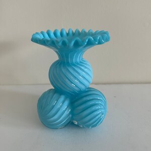 May include: A light blue glass vase with a ruffled top and a base made of three round, spiraled sections.