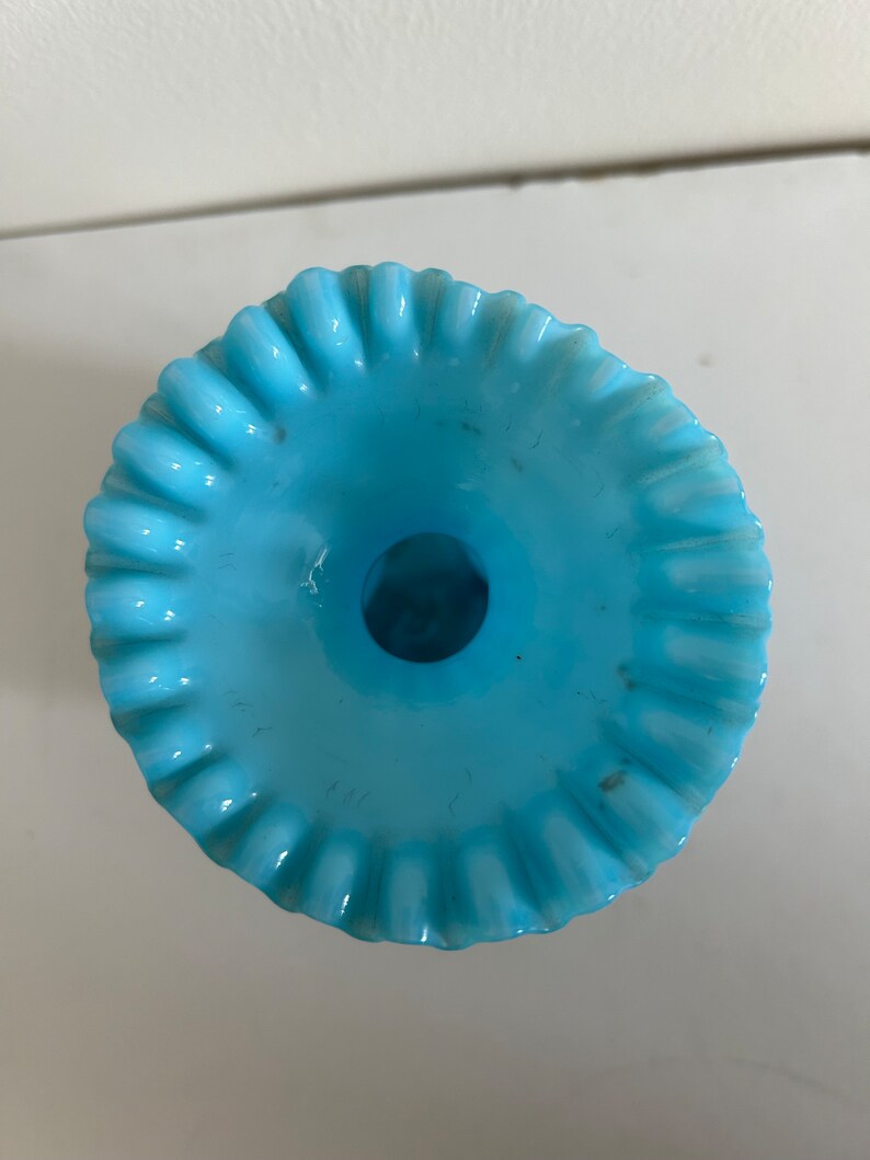 May include: A light blue glass vase with a ruffled rim. The vase has a wide opening and a narrow base.