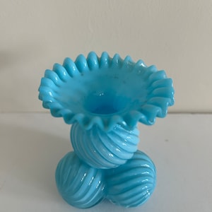 May include: A light blue glass vase with a ruffled top and a base made of three spiraled balls.