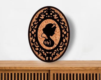 May include: An oval-shaped wall decor piece featuring a natural brown cork center and a black laser-cut frame. The frame displays an intricate, ornate scrollwork pattern surrounding a central black silhouette of a female figure in profile.