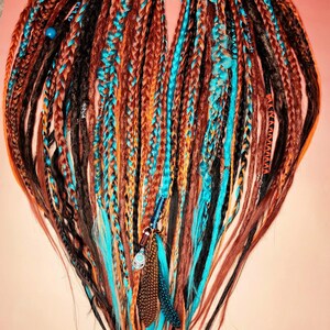 K&ouml;nnte beinhalten: Ein Satz synthetischer Dreadlocks in den Farben Braun, Schwarz, Orange und T&uuml;rkis. Die Dreadlocks sind oben zusammengebunden und haben Perlen und Federn angebracht.