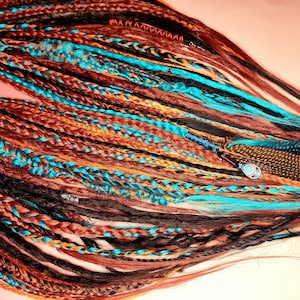 K&ouml;nnte beinhalten: Ein Set aus bunten synthetischen Dreadlocks mit braunen, schwarzen, orangen und t&uuml;rkisfarbenen Str&auml;hnen. Die Dreadlocks sind mit Federn und Perlen verziert.