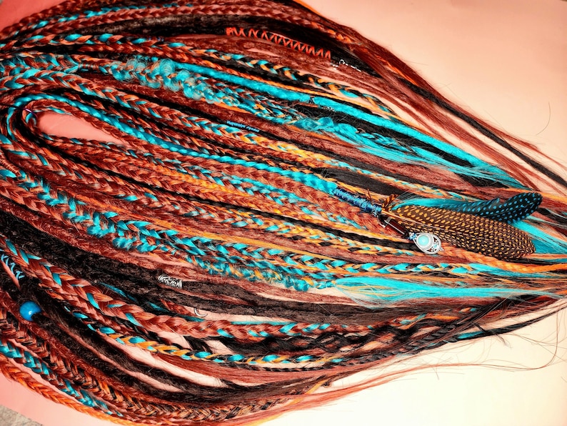 K&ouml;nnte beinhalten: Ein Set aus bunten synthetischen Dreadlocks mit braunen, schwarzen, orangen und t&uuml;rkisfarbenen Str&auml;hnen. Die Dreadlocks sind mit Federn und Perlen verziert.