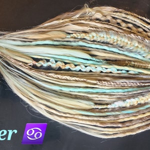 May include: A set of synthetic dreadlocks in shades of blonde, brown, and light blue. The dreadlocks are tied together at the end. The text "Cancer ♋" is visible in the bottom left corner of the image.