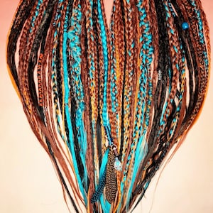 K&ouml;nnte beinhalten: Ein Satz synthetischer Dreadlocks in den Farben Braun, Schwarz, Orange und T&uuml;rkis. Die Dreadlocks sind oben zusammengebunden und haben Perlen und Federn angebracht.
