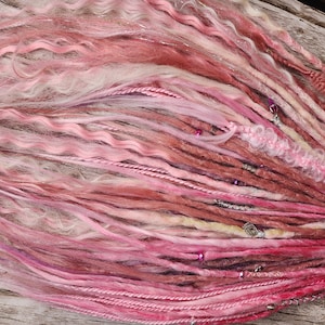 May include: Pink, white, and brown synthetic dreadlocks with beads and charms.