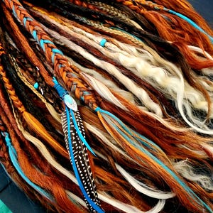 May include: A collection of handmade dreadlocks in various shades of brown, orange, and blonde. Some dreads are braided with turquoise accents and adorned with a blue and black feather. The dreadlocks are a bohemian style.