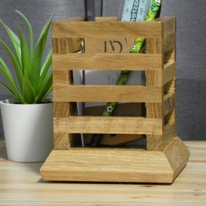 May include: A wooden desk organiser with four compartments. The organiser is made of light brown wood and has a natural finish. It is filled with pens, pencils, and a ruler.