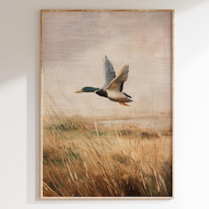 May include: A framed print of a duck in flight over tall grass. The artwork features a muted color palette with shades of brown, beige, and gray. The duck has green, brown, and white feathers. The artwork is in a wooden frame.
