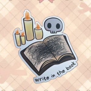 Könnte beinhalten: Ein Aufkleber mit einem Totenkopf, drei brennenden Kerzen und einem offenen Buch mit gekritzelten Seiten. Der Text "Write in the book" steht unter dem Buch. Der Aufkleber hat einen silbernen Rand und einen Cartoon-Stil.