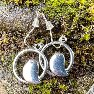 May include: Silver earrings with a circle design and a bird silhouette inside each circle.