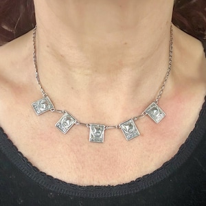 May include: Silver-toned necklace featuring five square pendants with a detailed design. The necklace is worn around the neck, showcasing the intricate craftsmanship of the jewelry. The chain is delicate, and the pendants are evenly spaced.