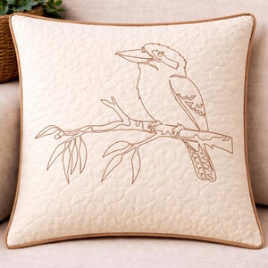 May include: Cream-coloured square cushion featuring a brown embroidered design of a bird on a branch with leaves. The cushion has a brown border and a quilted pattern. Ideal for home decor.